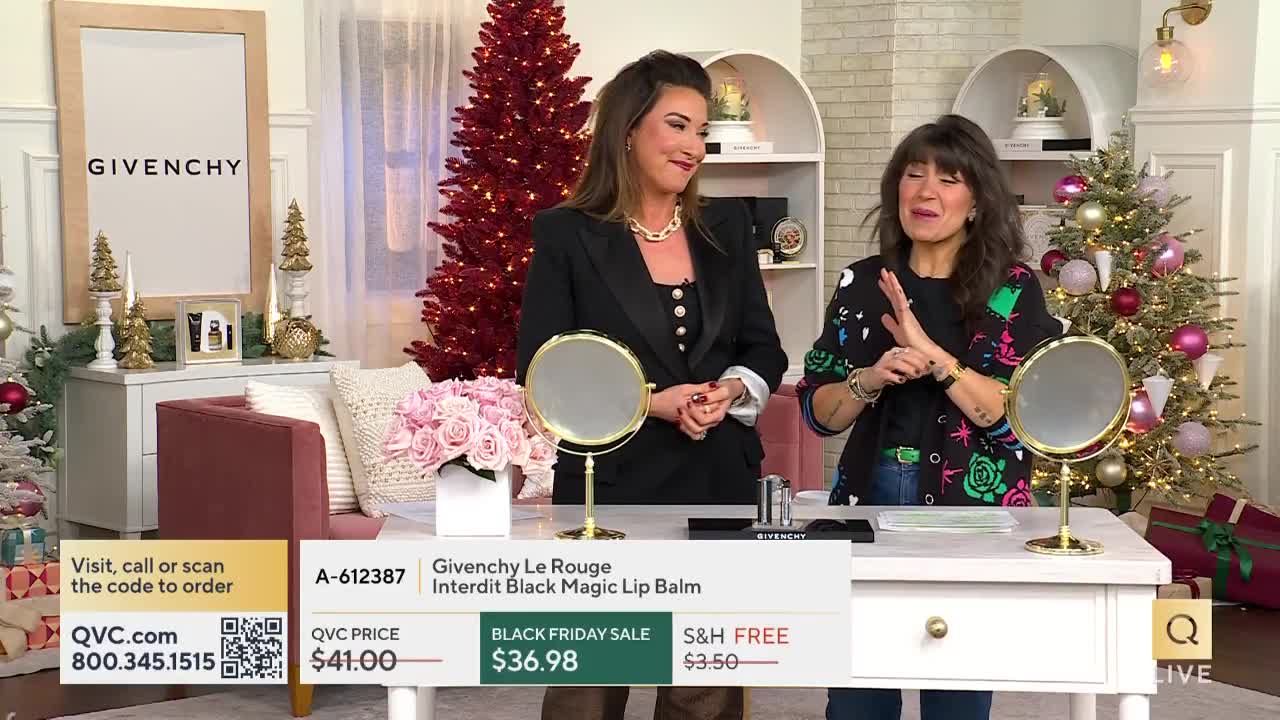 Two women stand at a table, gesturing and talking in a studio decorated for the holidays. A screen displays the price and details for a Givenchy lip balm, as seen on QVC.
