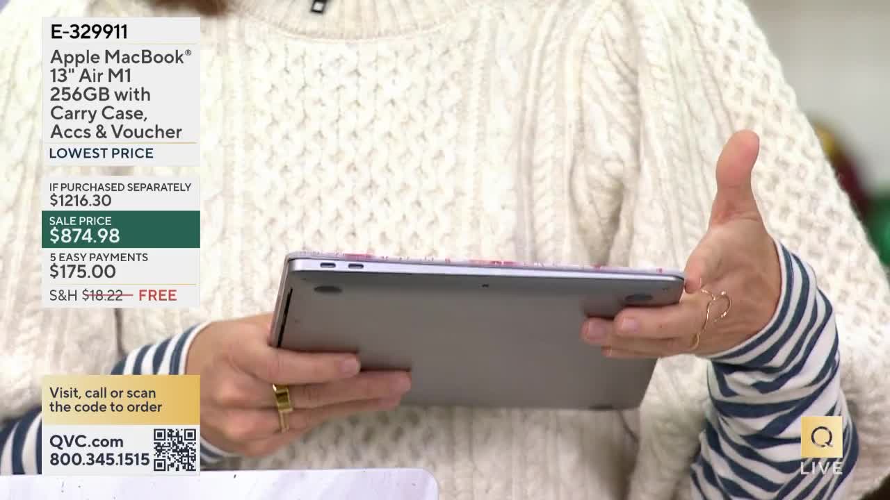 A person on QVC holds up a silver laptop, displaying its underside. The presenter's hand gestures towards the device, while a price tag graphic is visible on the left.
