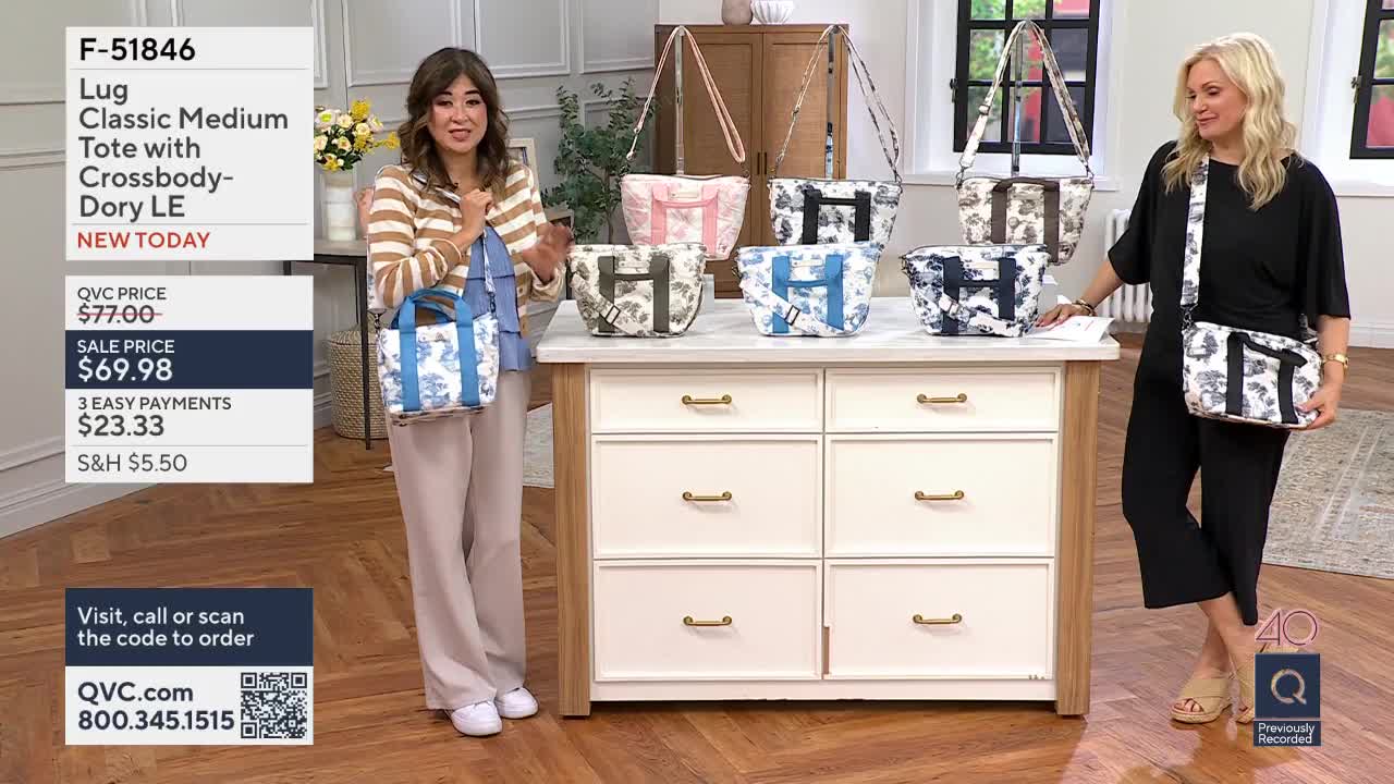 A woman holds up a blue and white patterned tote bag, gesturing with her free hand. Another woman stands to the right, wearing a black jumpsuit and a matching crossbody bag.