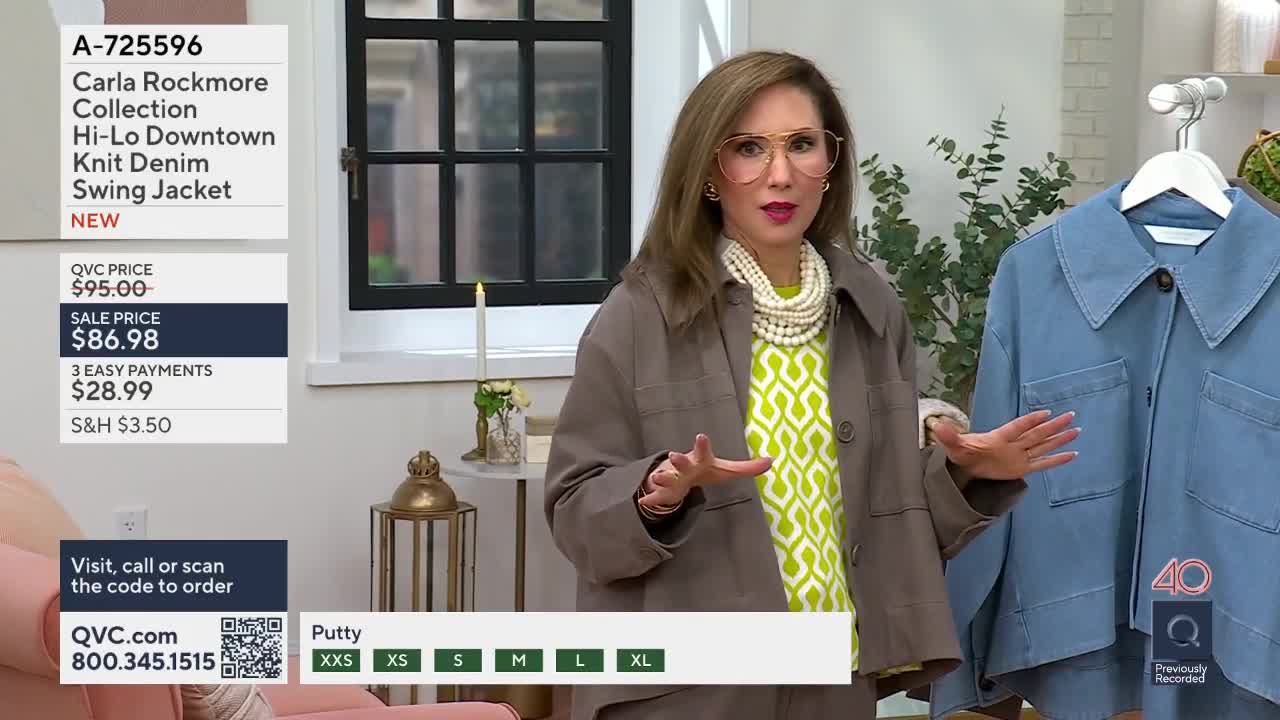 A woman in a taupe jacket gestures towards a light blue denim jacket hanging on a rack. On the screen, the QVC logo and pricing information for the jacket are displayed.
