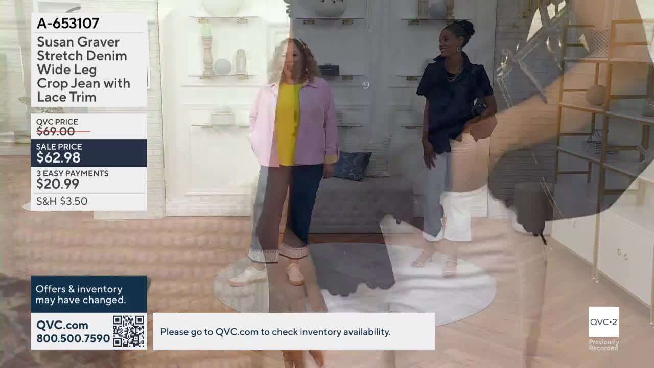 Two women stand on a set, one modeling denim jeans and a pink jacket, the other in a black top and white pants. The QVC2 logo is visible in the corner, and the product details are displayed on screen.

