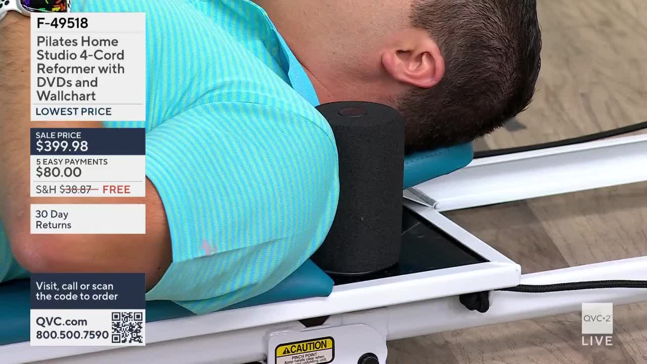 A man rests his head against a black cylindrical cushion on a white Pilates reformer. The QVC2 logo is visible in the corner, and the sale price for the equipment is displayed on screen.

