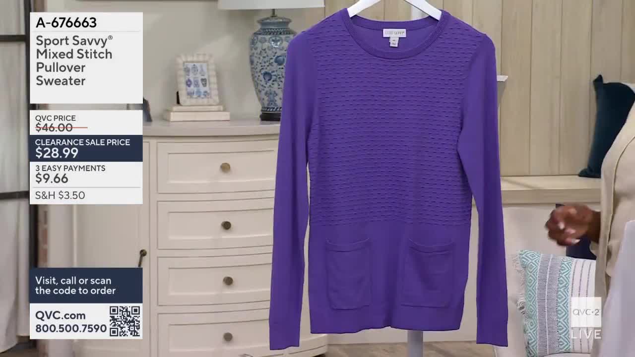A vibrant purple sweater hangs on a white hanger, displayed on a QVC2 set. The price and ordering information are visible on the left side of the screen.
