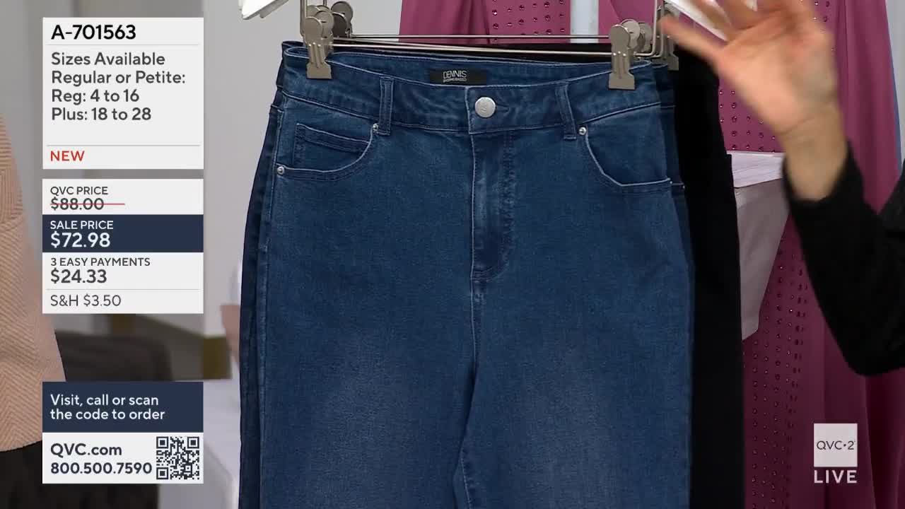A pair of blue jeans hangs from a metal hanger, displayed on a QVC2 set. A hand gestures towards the jeans, while the screen displays the item number and sale price.
