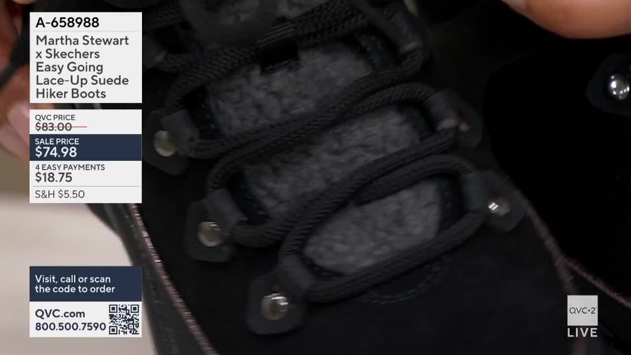 The camera focuses on the black laces and eyelets of a suede hiker boot. A QVC2 graphic displays the price and item details.
