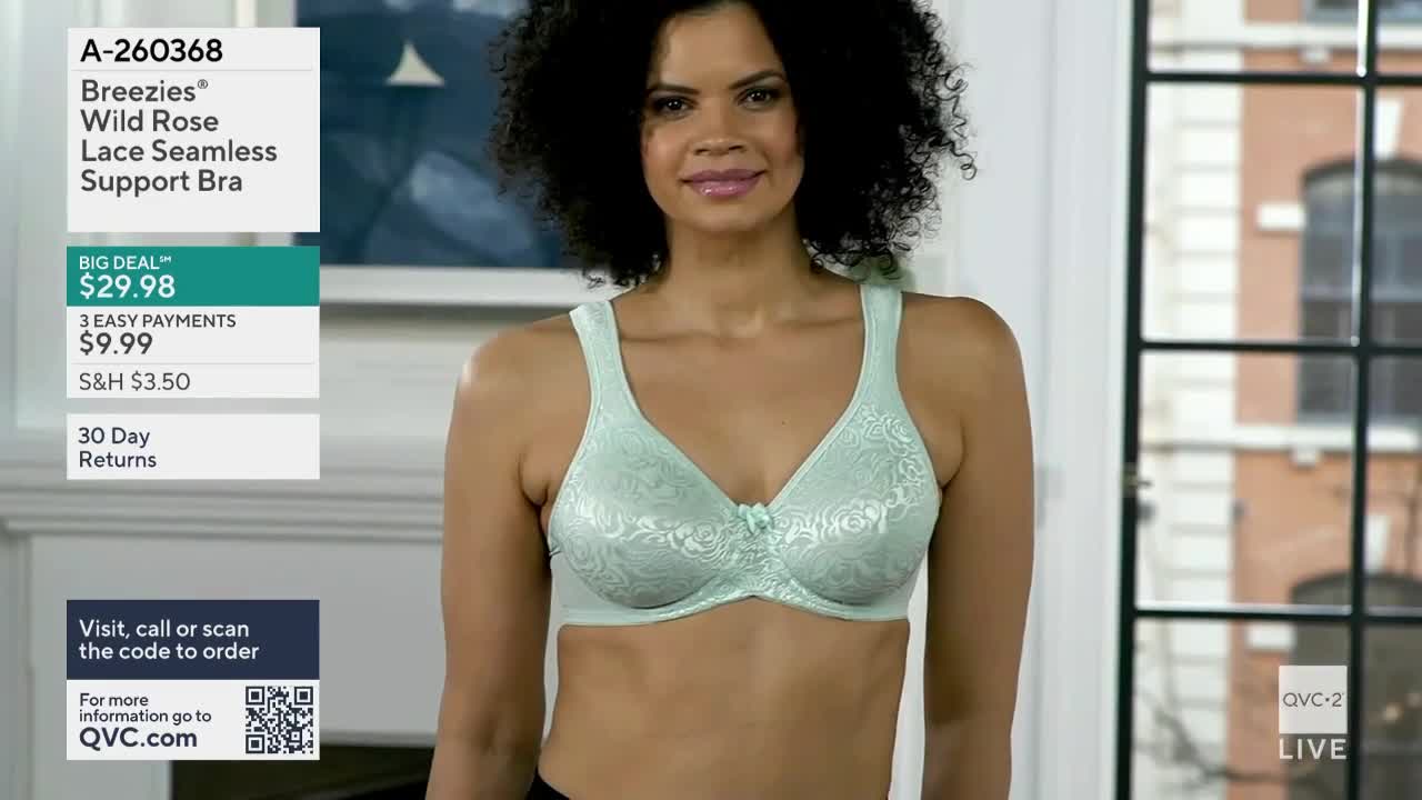A woman stands in a studio, modeling a mint green bra. The QVC2 logo and product information are visible on the screen.
