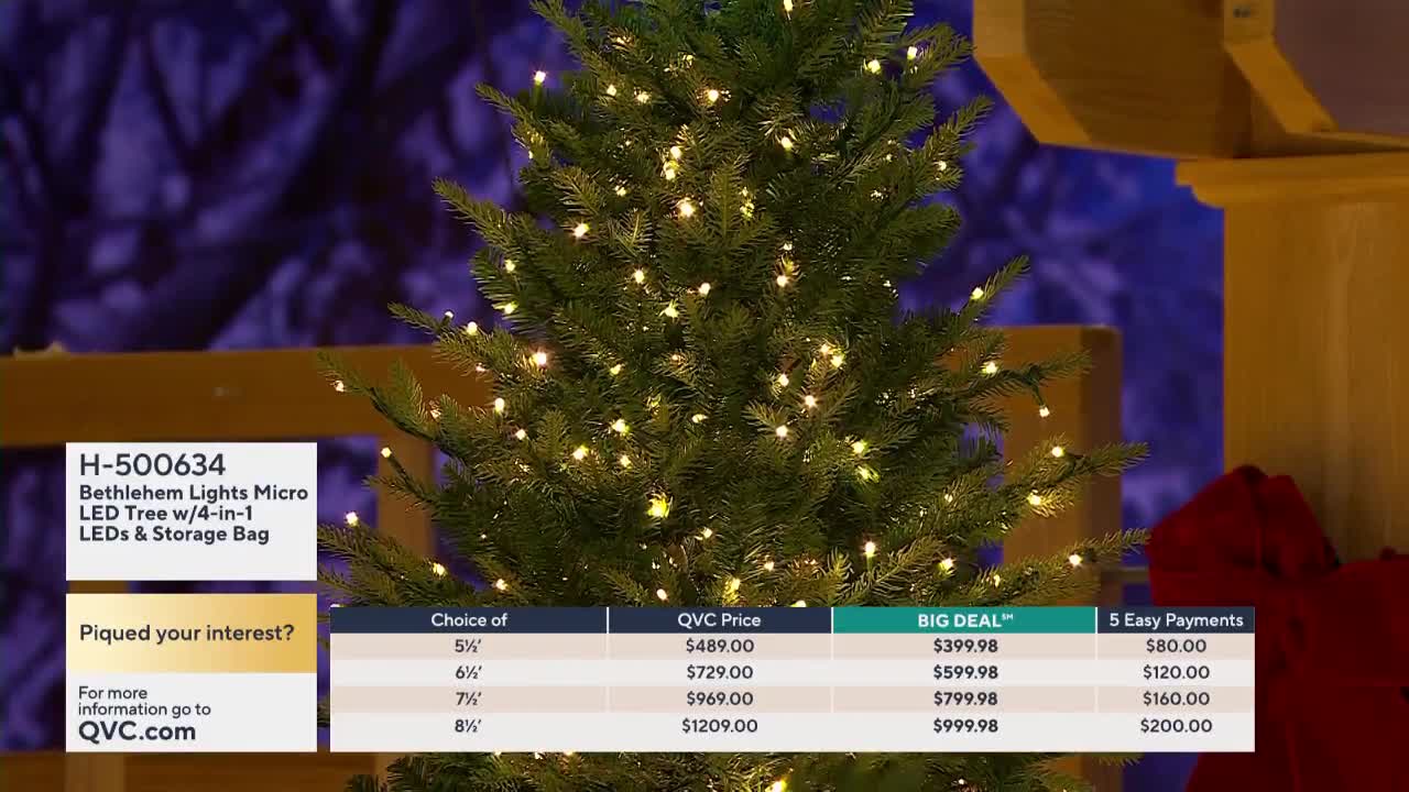 A lit-up artificial Christmas tree stands center stage, its tiny lights twinkling against a deep blue backdrop. Below, a QVC2 graphic displays the tree's price and payment options.
