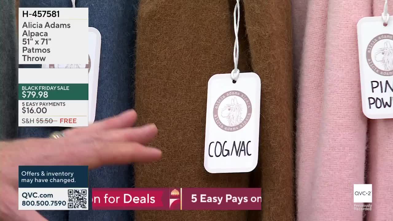 A hand gestures towards a row of soft, textured throws hanging on display. Each throw has a tag, with the "Cognac" one prominently featured.
