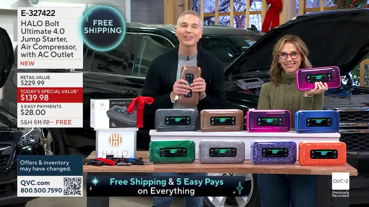 A man and woman on QVC2 are holding up different colored HALO Bolt jump starters. Behind them, a car's hood is open, and a table displays several more of the devices.
