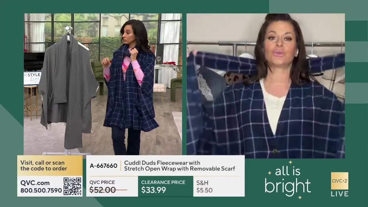 A woman on QVC2 in the United States holds up a navy and white plaid wrap, showing the camera how it drapes. Across the screen, another woman models a similar wrap, and a rack displays a gray version.
