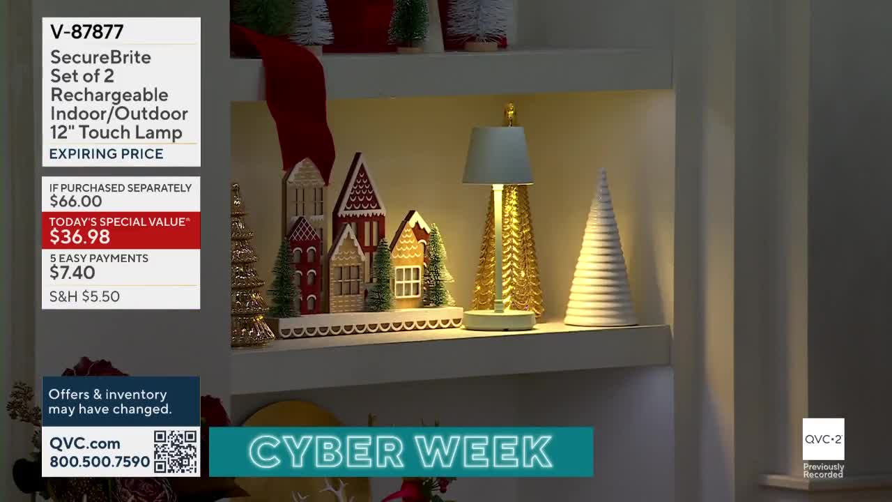 A decorative lamp, shaped like a golden Christmas tree, sits on a shelf alongside a miniature village. The QVC2 graphic in the corner highlights a "Cyber Week" special on the lamp.
