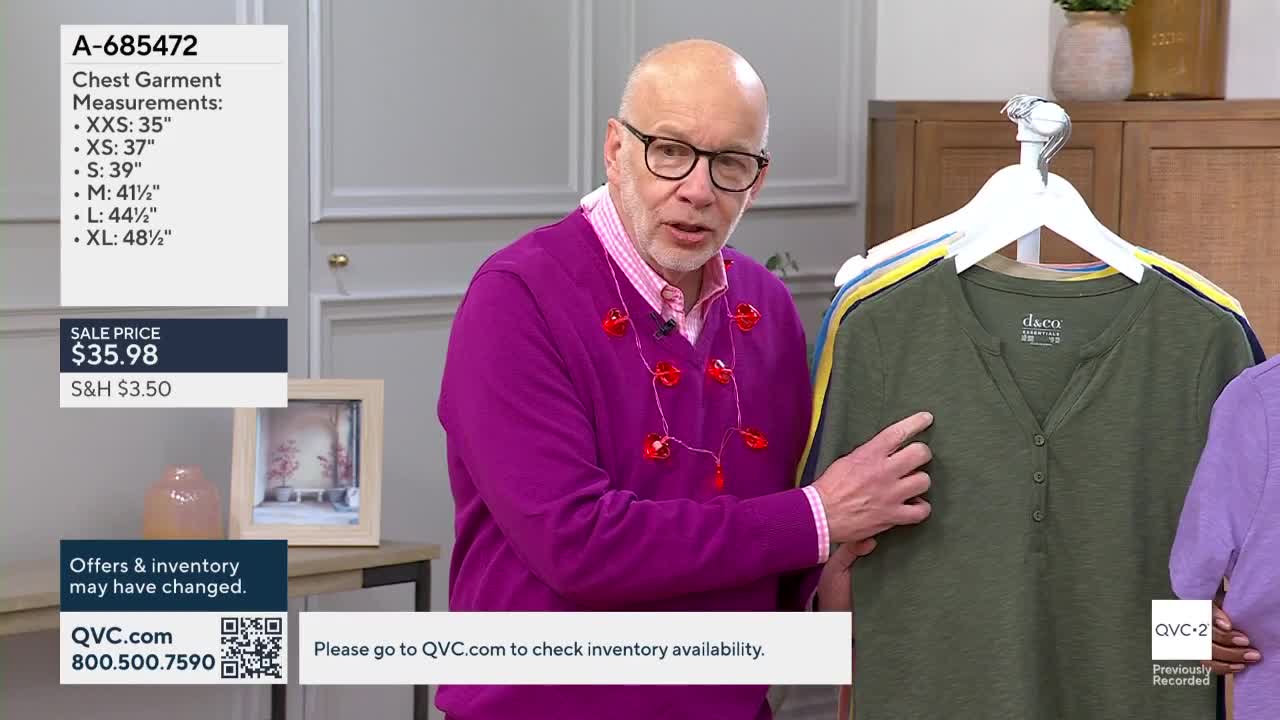 A man in a bright purple sweater points to a green henley shirt hanging on a rack. Another person in a purple shirt stands to his right.