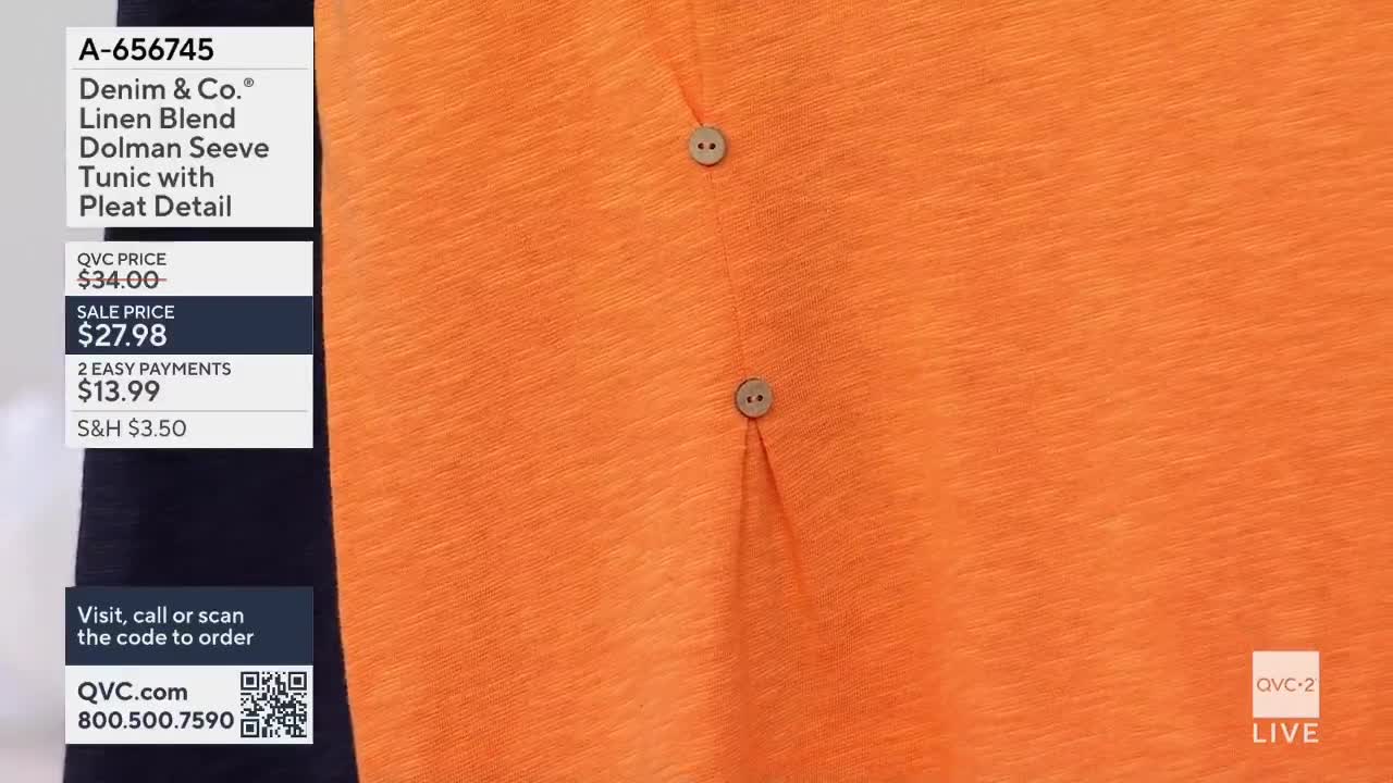 The bright orange fabric of a tunic is displayed, featuring two small, round buttons and a subtle pleat. A graphic overlay lists the item's price and ordering information for QVC2.