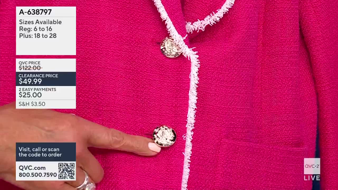 A finger points to a large, ornate button on a bright pink jacket. The QVC2 logo appears in the lower right corner.