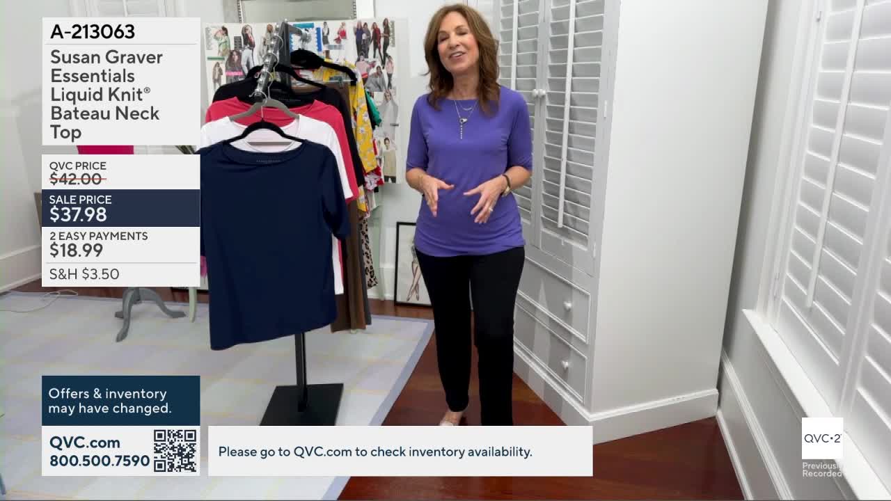 A woman in a purple top and black pants stands beside a rack of colorful shirts. A navy blue t-shirt hangs on a display stand in front of her.