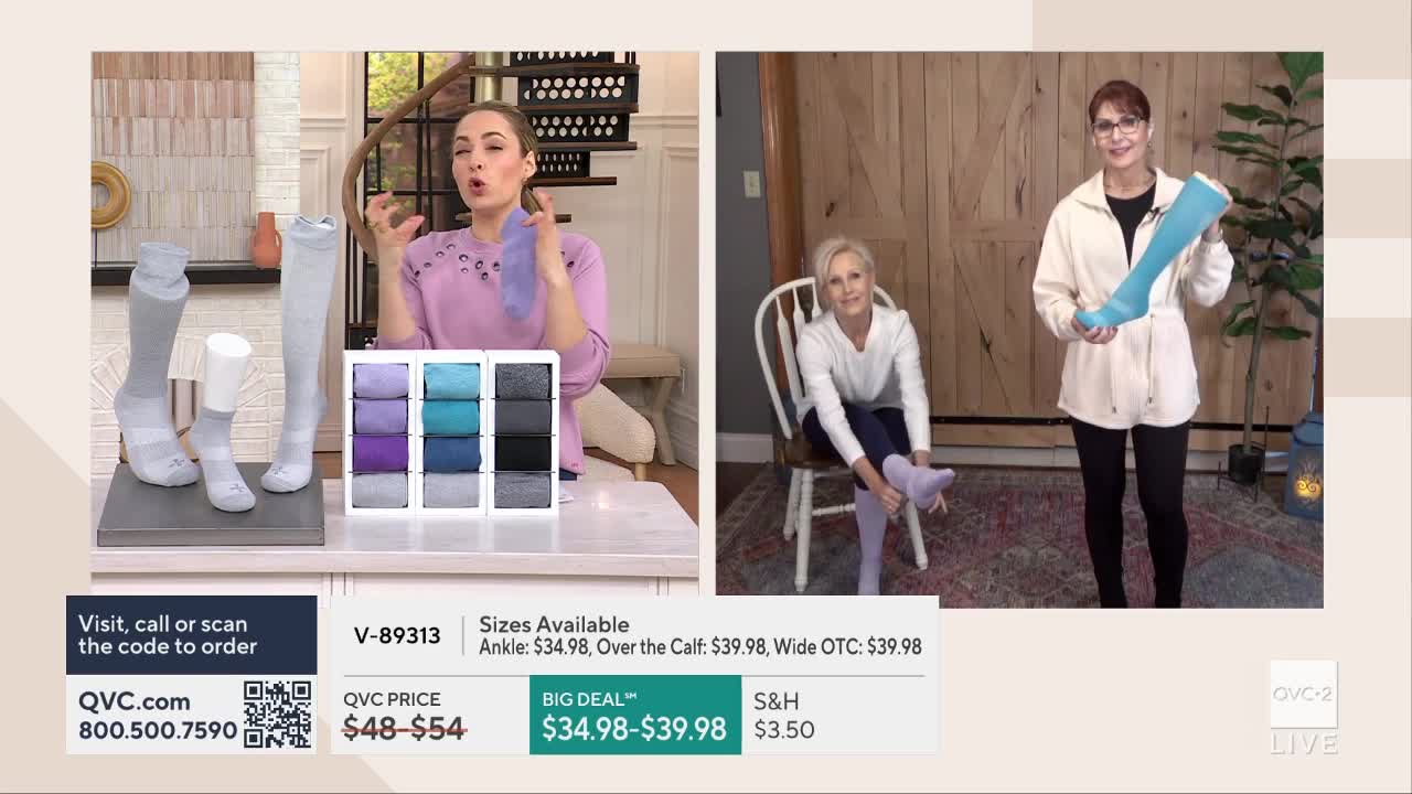 A woman on QVC2 holds up a pair of light blue compression socks. Another woman, seated, pulls a similar sock onto her foot.