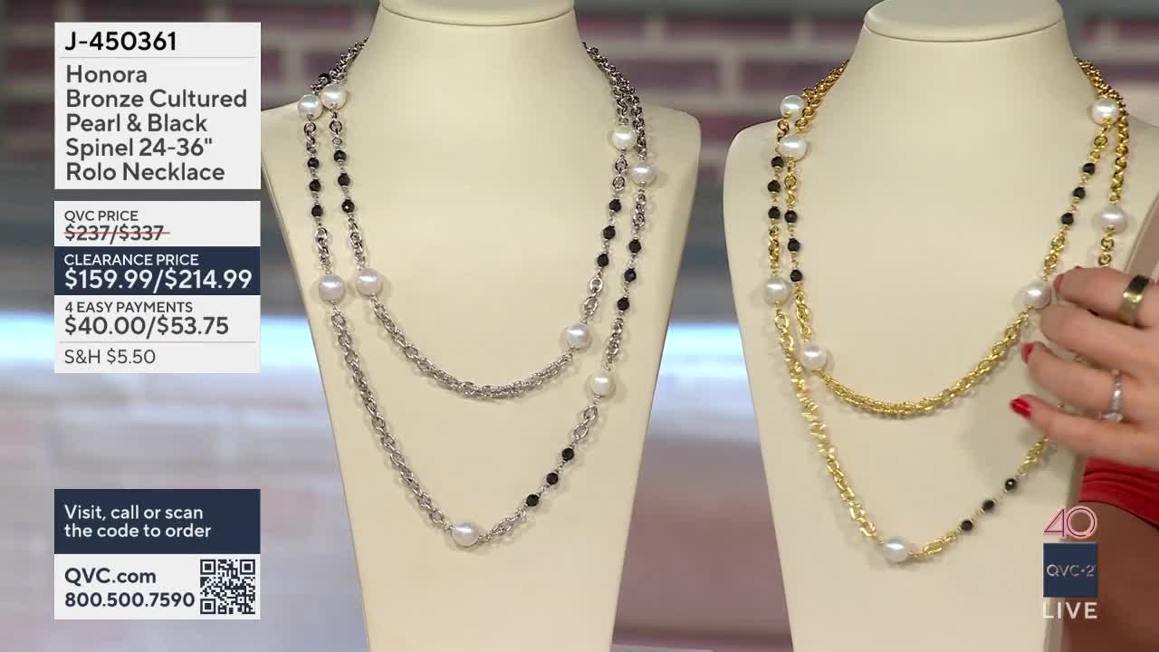 A hand with rings adjusts a long, layered gold necklace with pearls and black beads. The necklace is displayed on a mannequin alongside a similar silver version.