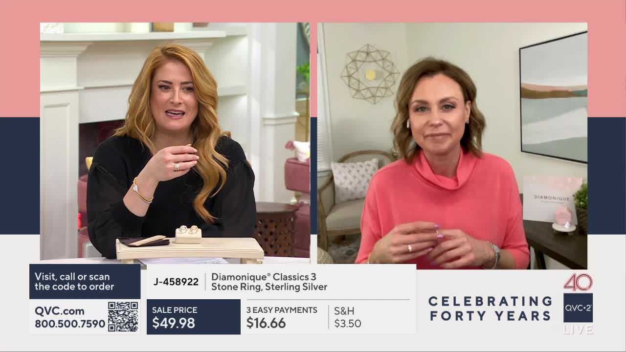 A woman with long auburn hair gestures with her right hand, holding a small ring. Across from her, a woman with short brown hair smiles and fiddles with her own ring.