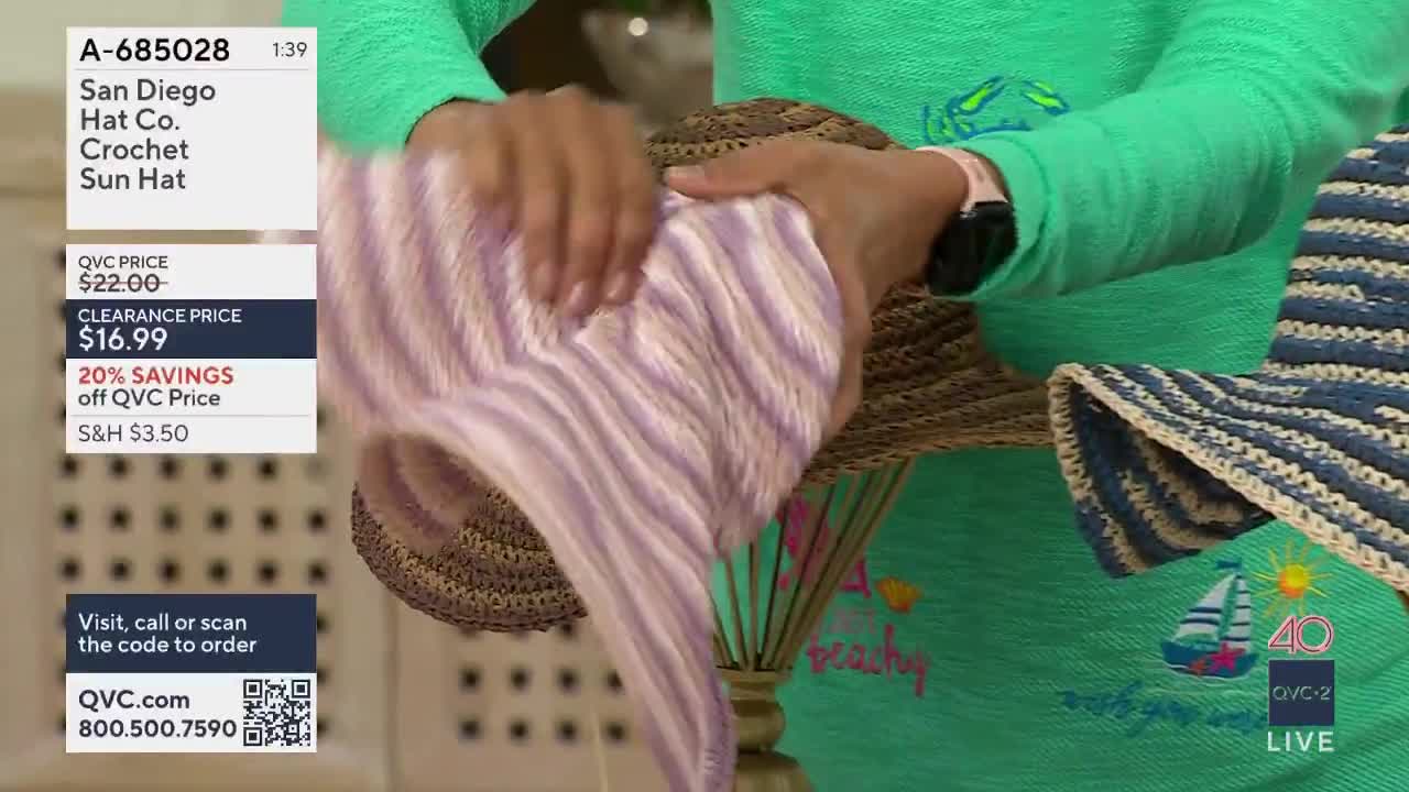 Hands smooth a striped fabric over a straw hat. Another crocheted hat, blue and white, sits to the right.