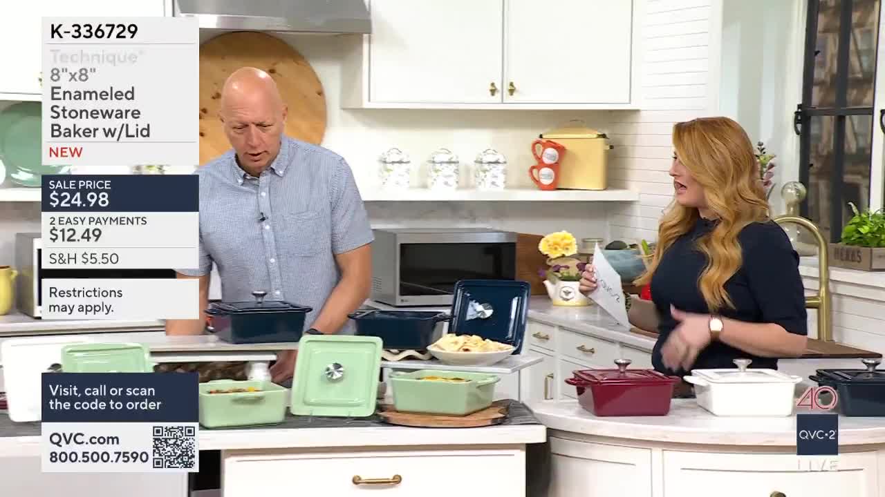 A man in a striped shirt gestures towards a dark blue baker on display. A woman with long, wavy red hair holds up a piece of paper, her other hand resting on a white baker.