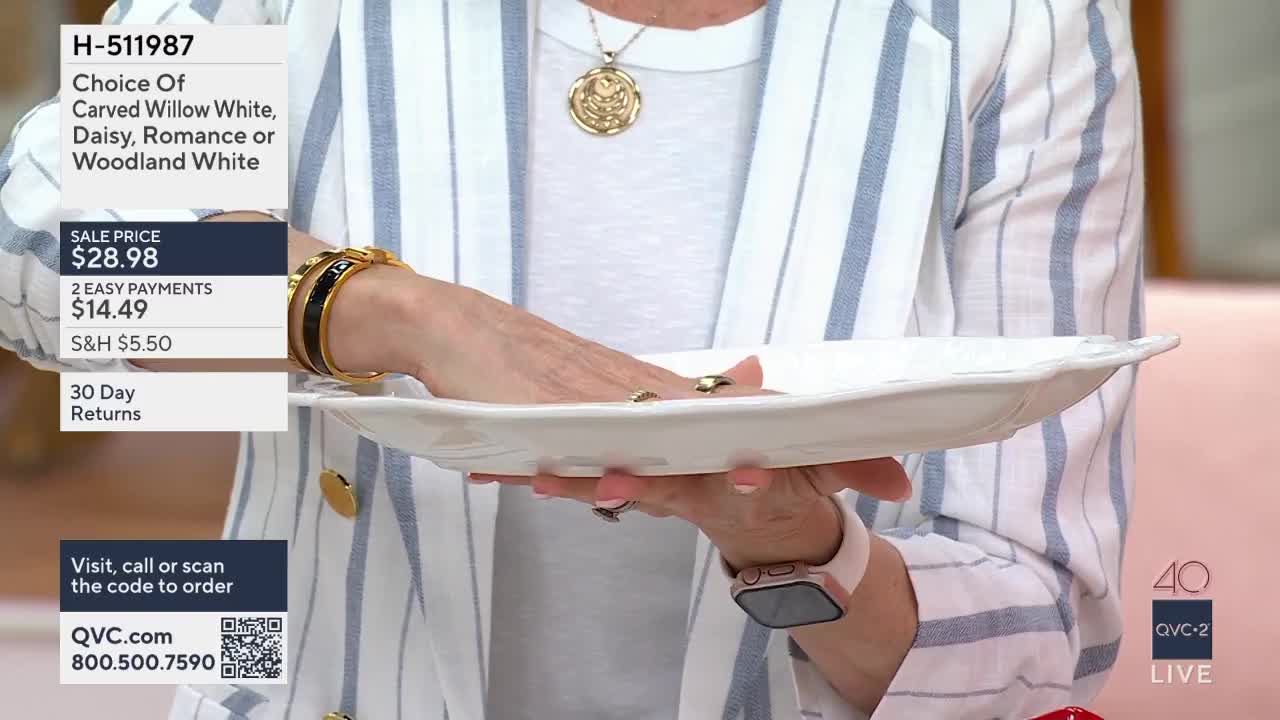 A woman's hands cradle a white, scalloped-edge plate. The QVC2 logo is visible on the right.