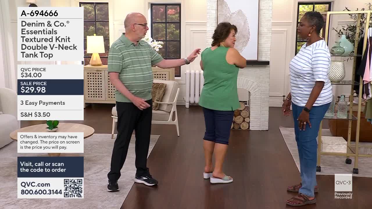 A man in a striped shirt gestures towards a woman in a green tank top, as she turns to face another woman in a striped shirt and jeans. The set is lit for a QVC3 segment, with a product description displayed on the left.
