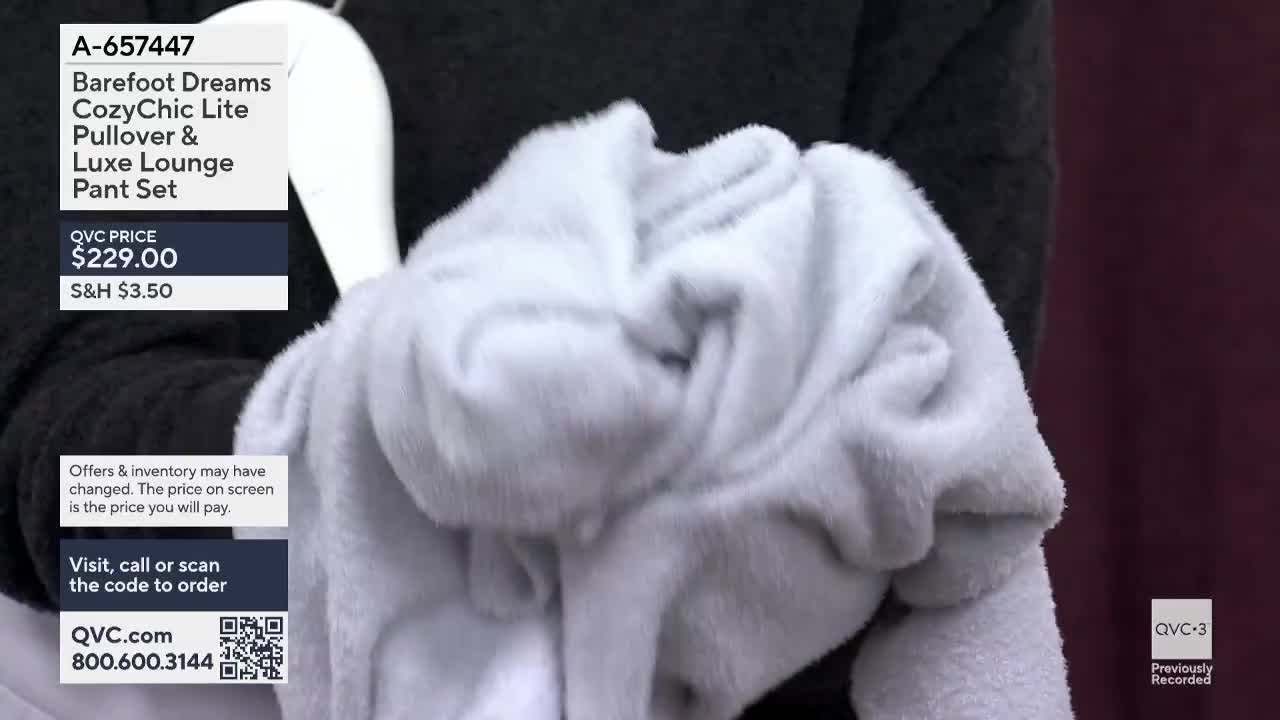 A fluffy white garment is held up, its texture prominent against a dark background. The QVC3 screen displays the price and item details for a Barefoot Dreams lounge set.
