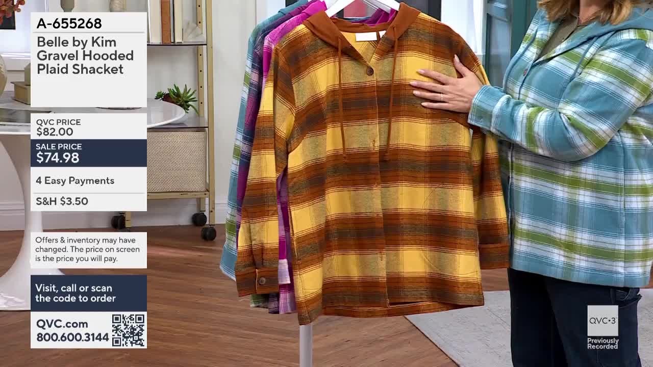 A woman in a blue and green plaid jacket touches a brown and yellow plaid shacket hanging on a rack. The QVC3 studio is showing the item for sale, listing the price and payment options.
