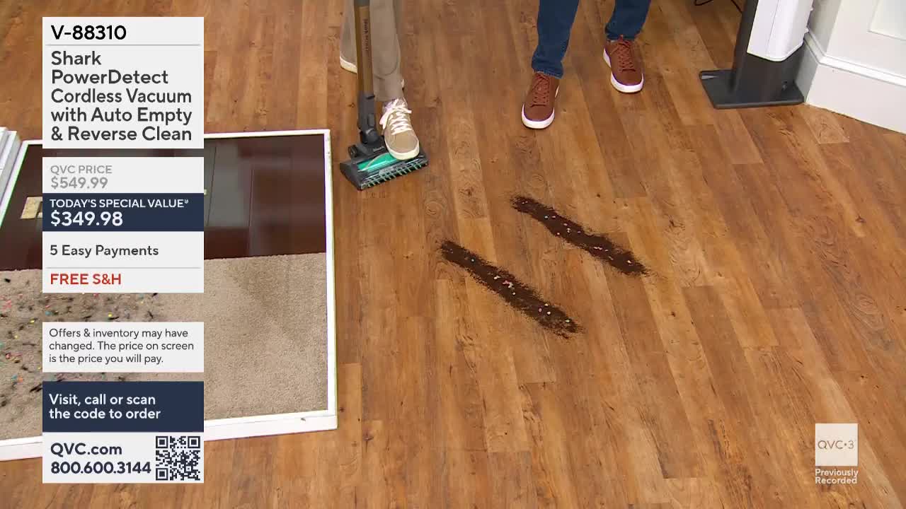 A person is demonstrating a vacuum cleaner on a wooden floor, cleaning up two dark, irregular streaks of something. The QVC3 logo is in the corner, and a product description is visible on the left.

