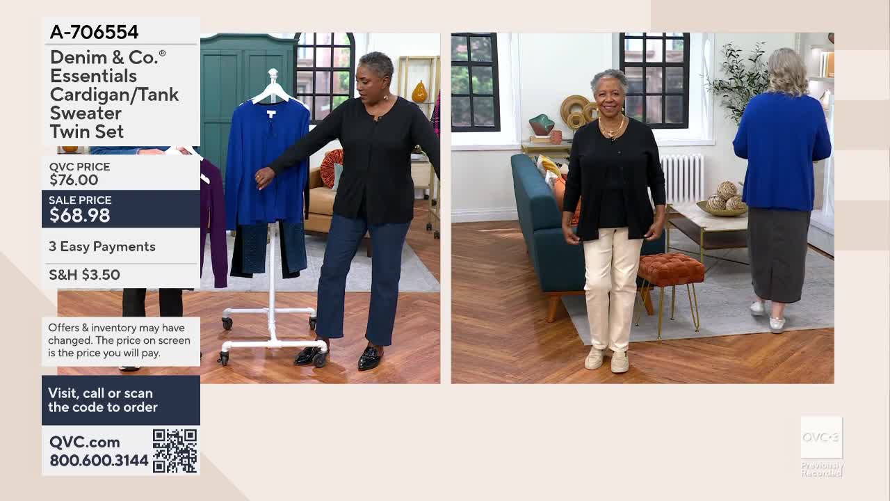 A woman in a black sweater and blue jeans gestures toward a rack of clothing on a QVC3 set. Another woman, wearing a similar sweater but with white pants, stands nearby.
