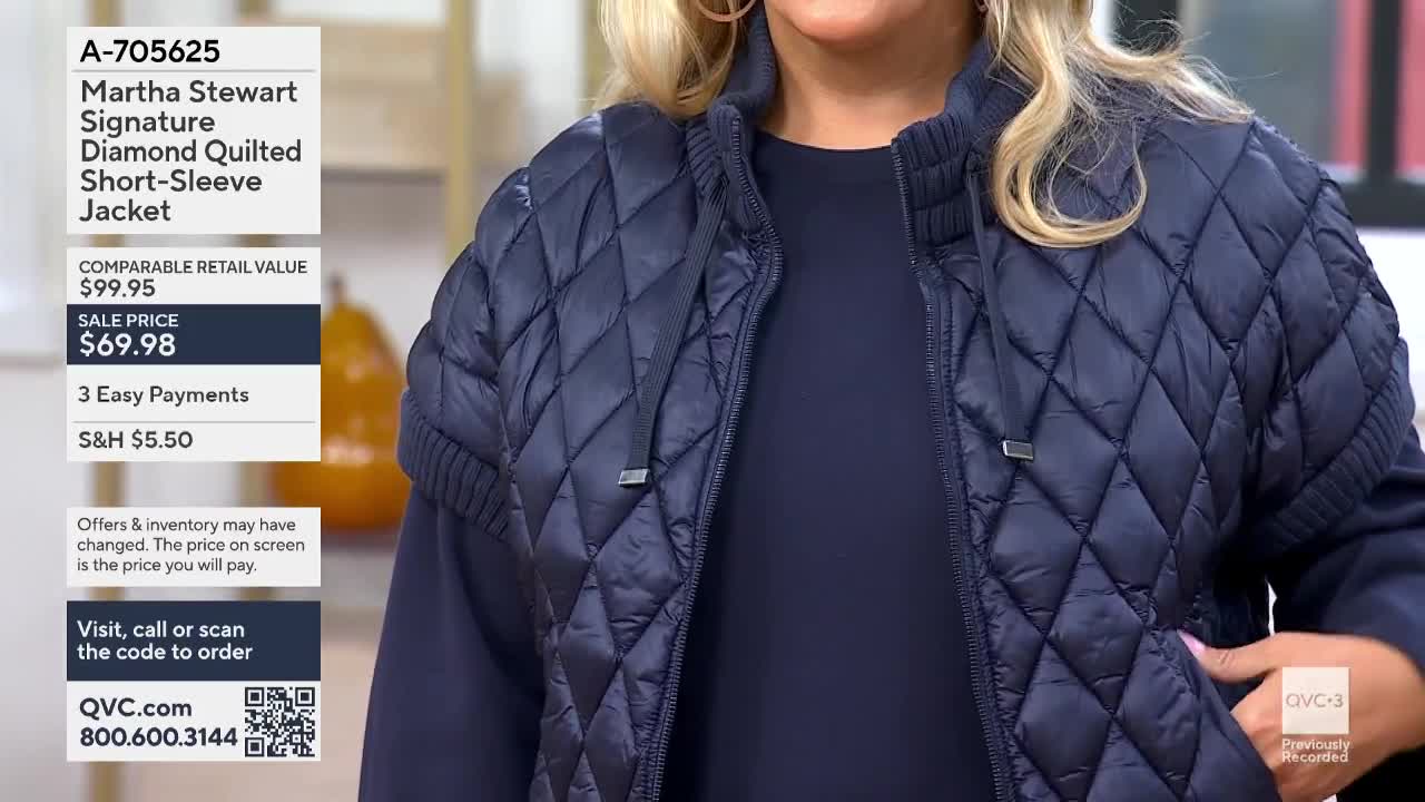 A woman in a navy quilted jacket stands on a QVC3 set, her hand resting in the pocket. The screen displays the jacket's price and item number.
