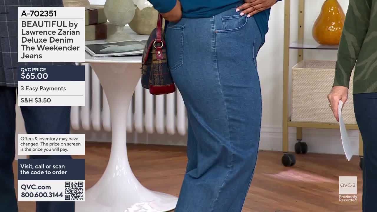 A woman in blue jeans stands with her hand in her pocket, showcasing the denim on QVC3. Beside her, another person holds a paper, ready to discuss the product.
