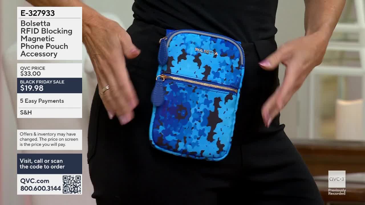 A woman wearing black pants and a black top has a blue and black patterned phone pouch attached to her waist. She's holding her hands near her hips, as if to show off the accessory on QVC3.
