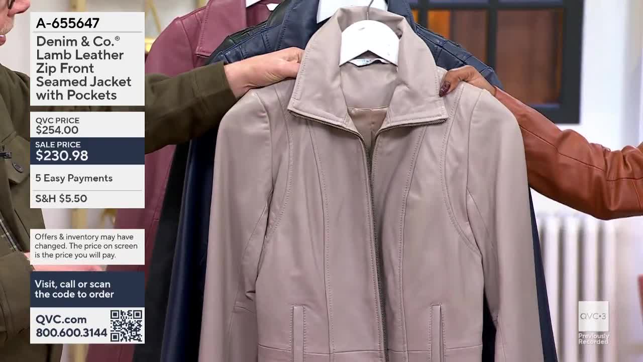 A woman holds up a light beige leather jacket, showing off the zip front and pockets. Other colored jackets hang behind it, and the price is displayed on the screen of QVC3.
