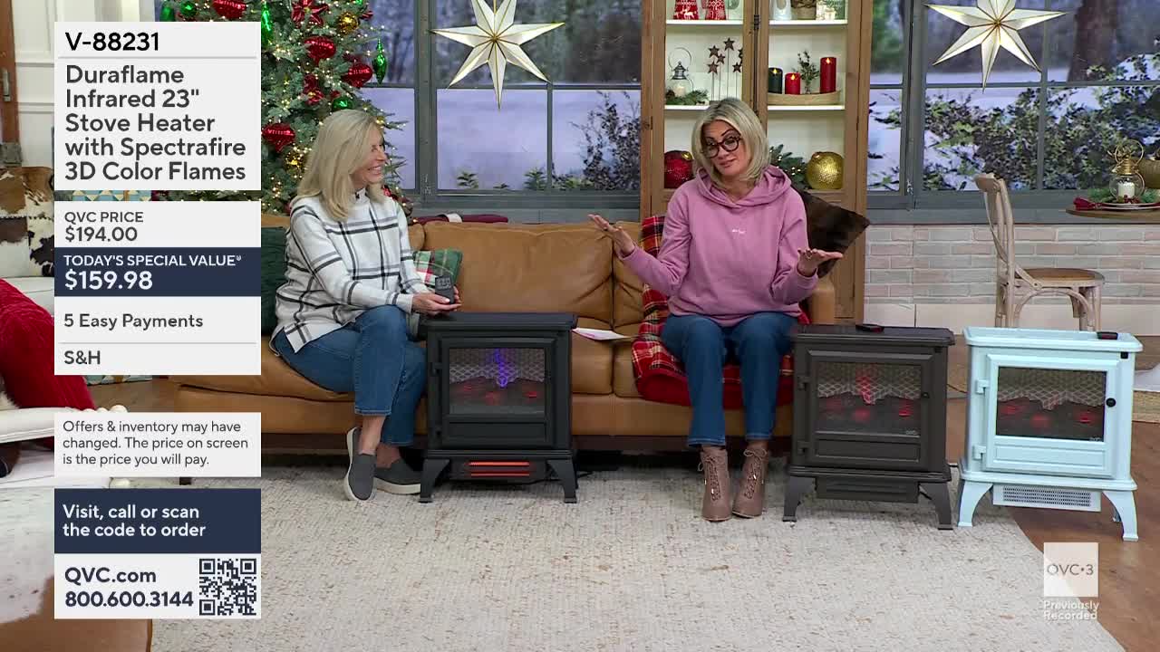 Two women on QVC3 are seated on a couch, demonstrating stove heaters. One gestures towards the heaters with open palms while the other holds a small box.
