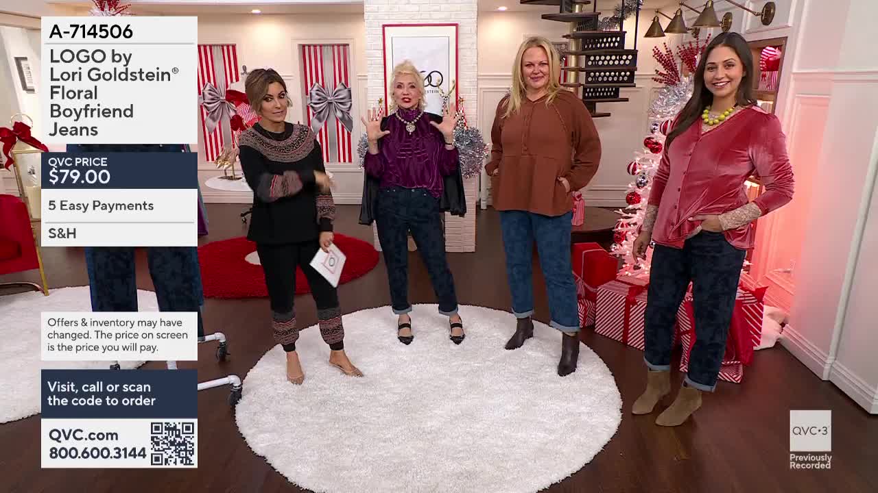 Four women stand on a white rug, showcasing jeans on a QVC3 set. One woman gestures with her hands, while the others pose, each wearing a different top.
