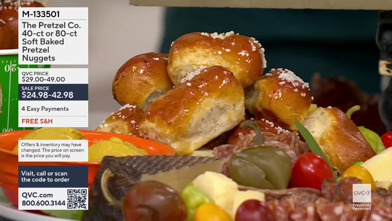 A pile of golden-brown pretzel nuggets, sprinkled with coarse salt, sits atop a platter of charcuterie. The QVC logo is visible in the lower right corner.