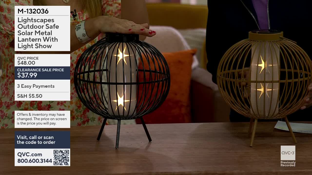 A hand hovers over a black, spherical lantern with a wire cage, its inner light glowing with star shapes. To its right, a similar golden lantern stands, also lit from within.
