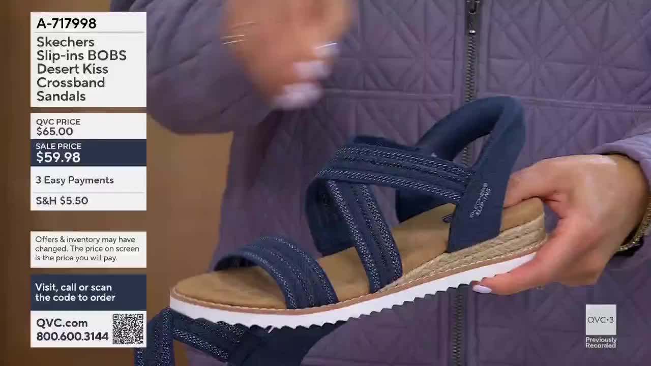 A hand adjusts a navy blue Skechers sandal with crisscrossing straps. The shoe has a tan espadrille-style sole and a white rubber bottom.