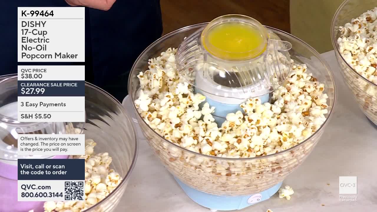 A light blue popcorn maker is overflowing with fluffy popcorn, with a small pool of melted butter at the top. Another bowl of popcorn sits to the right, nearly full.