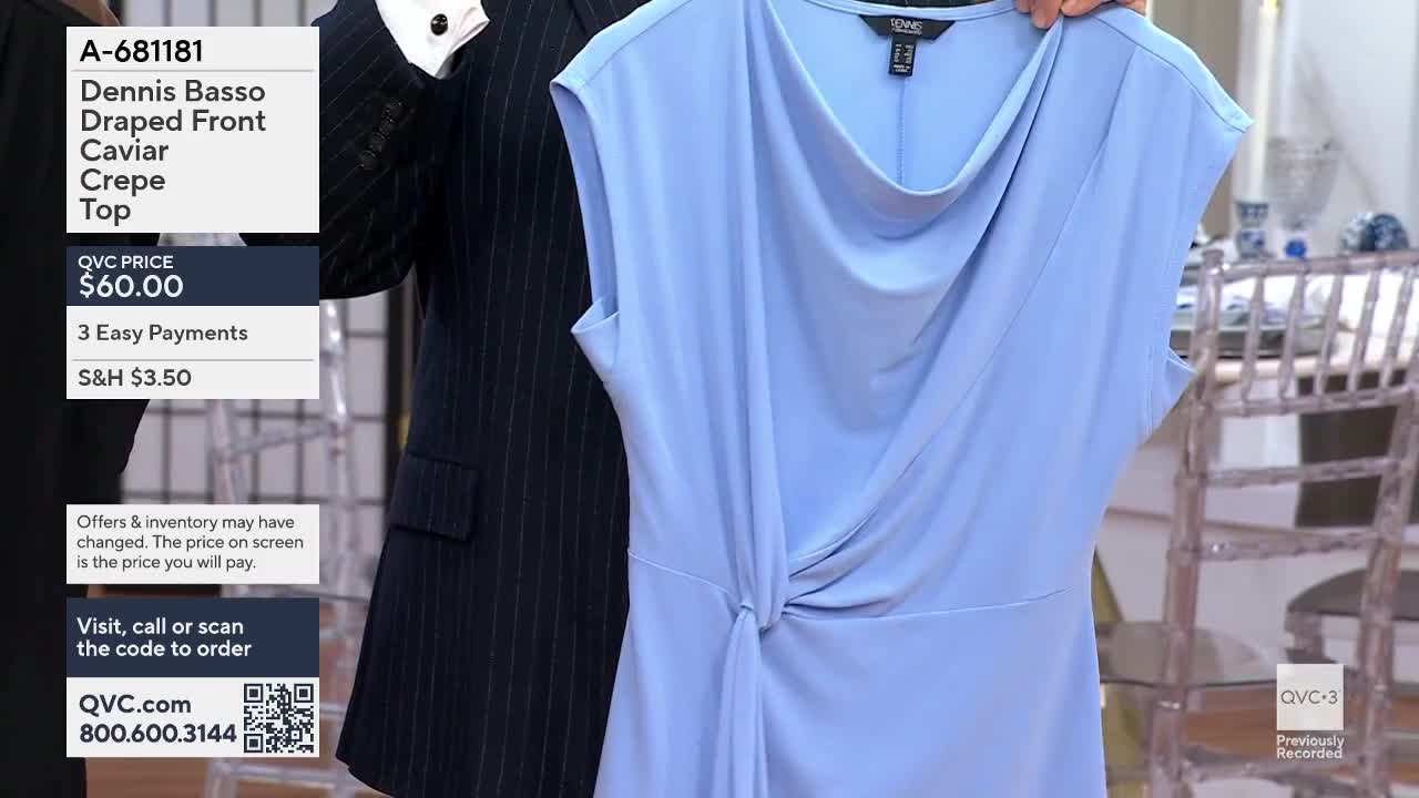 A man in a pinstripe suit holds up a light blue, draped top. The fabric drapes elegantly around the neckline and twists at the waist.