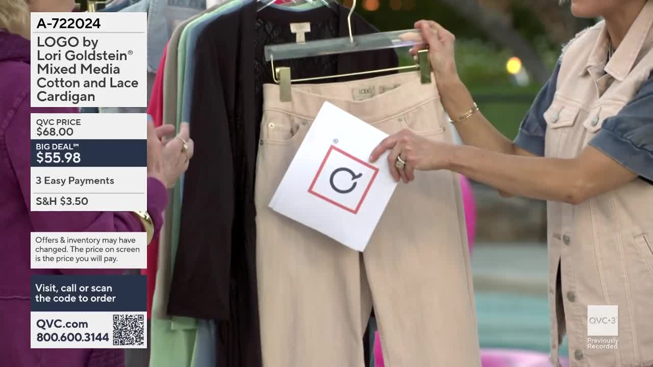 A woman holds up a card with a red square and a circular arrow logo in front of a pair of light-colored pants. Another woman stands nearby, adjusting the hanger of a black cardigan.