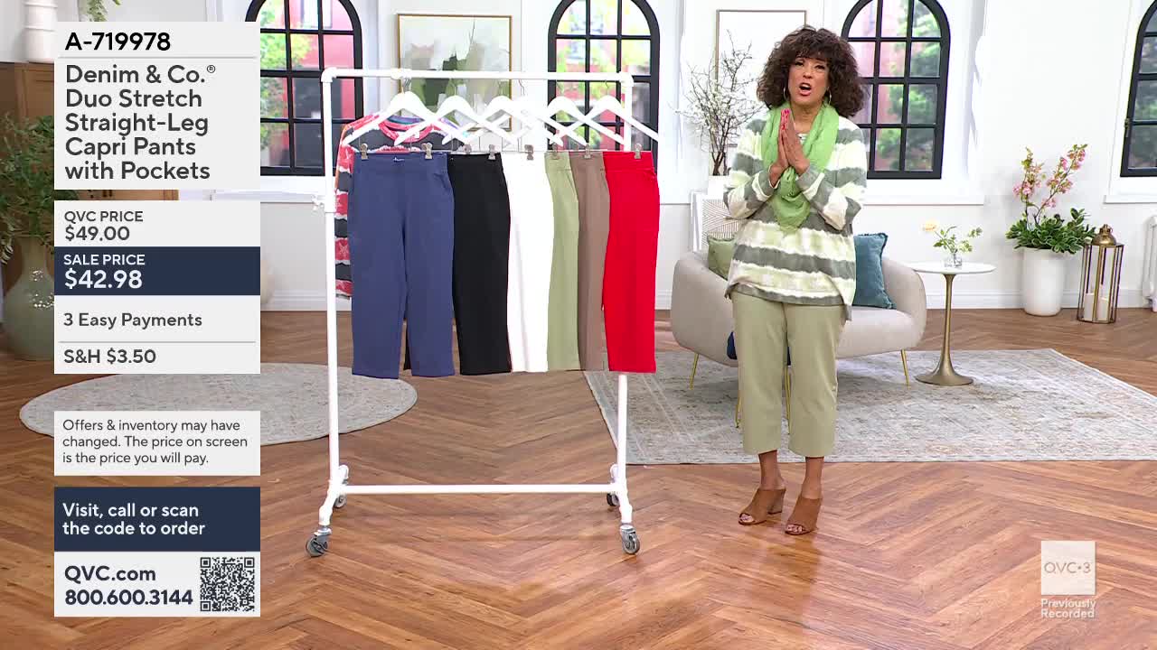 A woman in a striped top and green pants stands with her hands clasped, presenting a rack of colorful capri pants. The pants hang neatly in shades of blue, black, white, green, tan, and red.