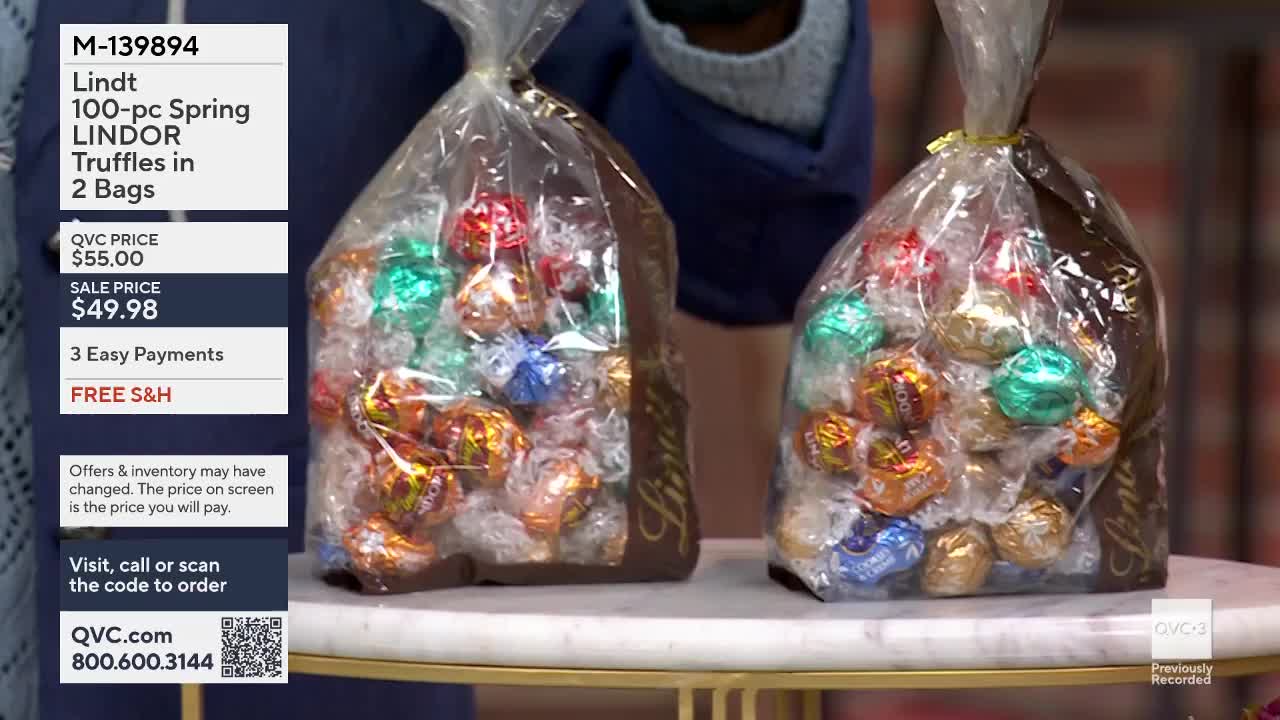 Two large, clear plastic bags overflow with individually wrapped Lindt chocolate truffles. The foil wrappers gleam in shades of red, blue, green, and gold, nestled together on a marble surface.