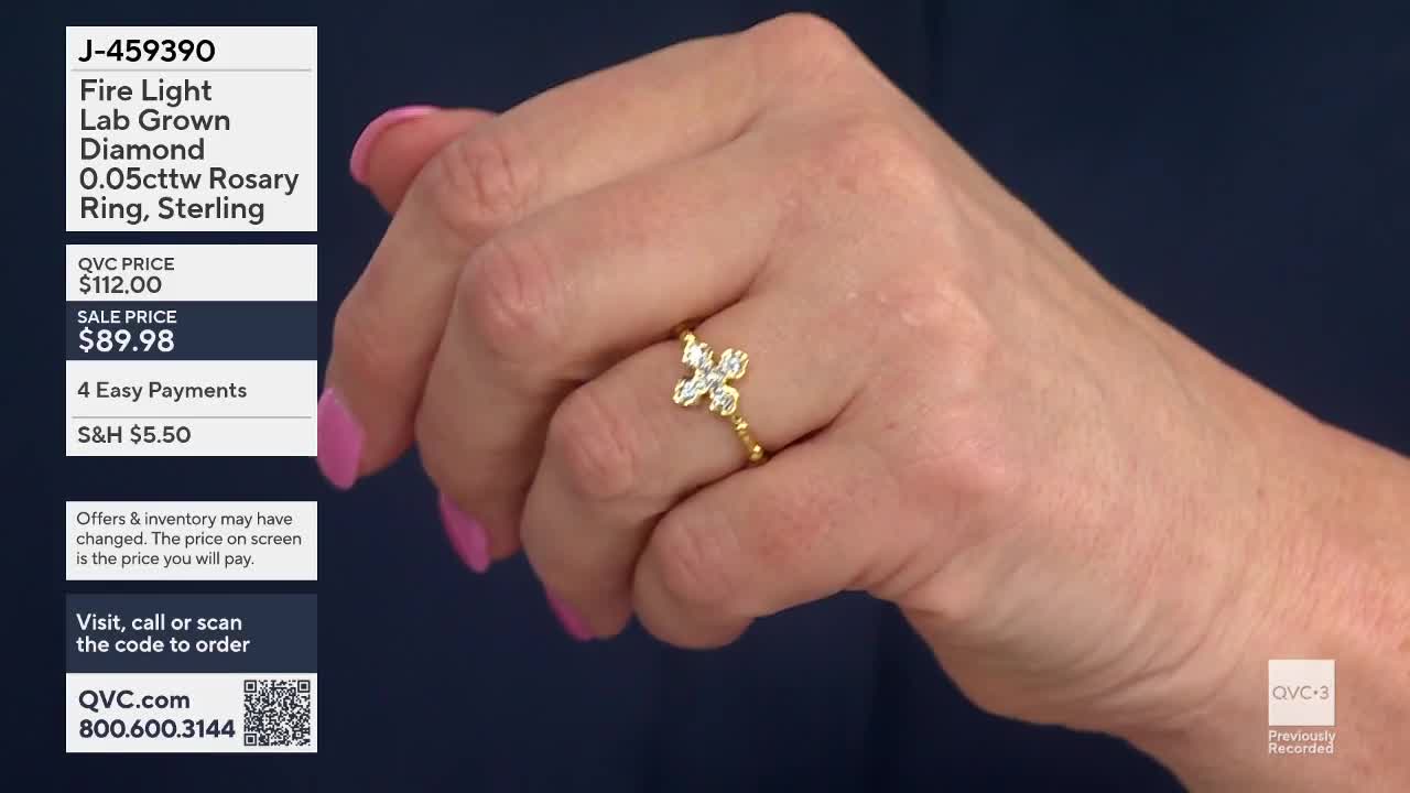 A hand displays a delicate gold ring featuring a cross-shaped diamond centerpiece. The ring's band is adorned with tiny golden beads.