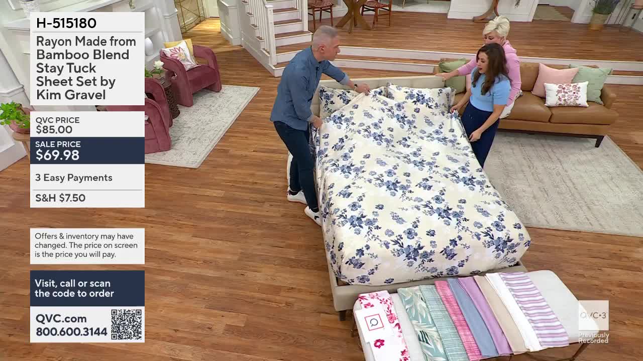 A man and a woman are pulling a floral-patterned sheet over a bed. The QVC logo is visible in the lower right corner.