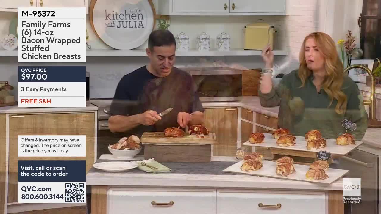 A man is slicing a bacon-wrapped chicken breast on a wooden board. A woman stands nearby, gesturing with her hand as she speaks.
