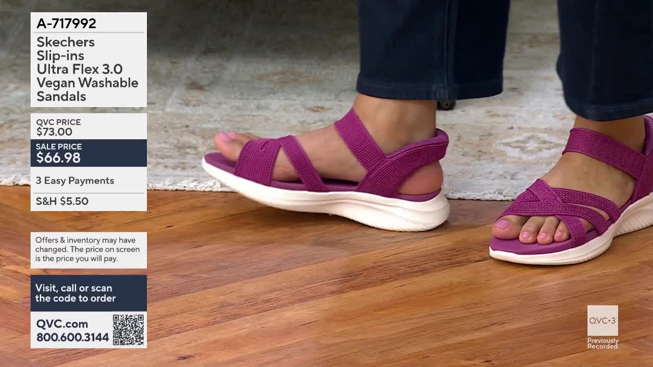 A foot lifts slightly, showing off a woven purple sandal with a white sole. Another sandal rests on the wooden floor, its straps crossing over the toes.