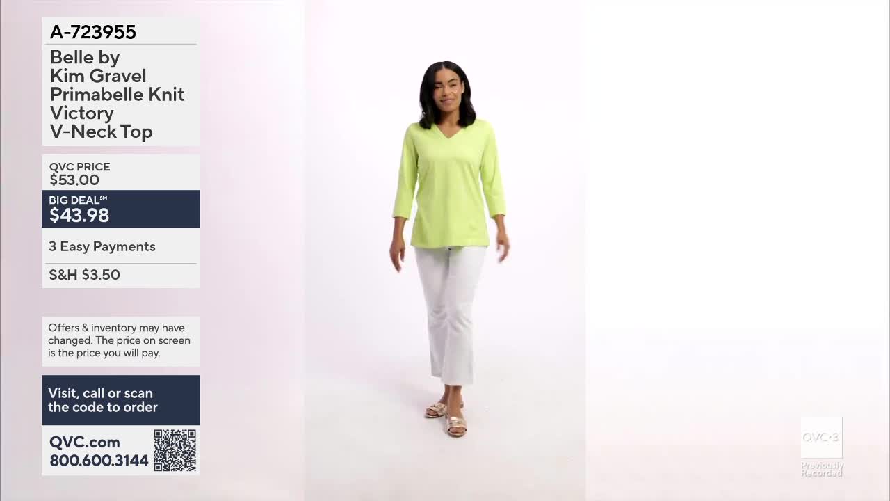 A woman walks toward me, modeling a bright green V-neck top and white pants. The QVC logo and item details are displayed on the left side of the screen.