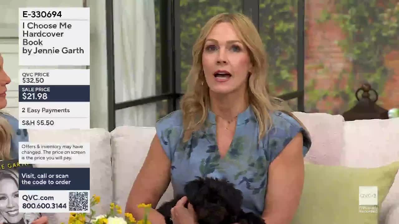 A woman with blonde hair, wearing a blue floral dress, speaks animatedly while holding a small black dog. On the left, a graphic displays the title "I Choose Me Hardcover Book by Jennie Garth" and pricing details for QVC.